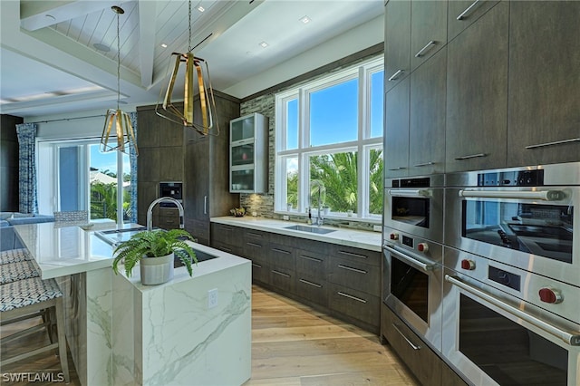 kitchen featuring light hardwood / wood-style flooring, a center island with sink, beamed ceiling, sink, and pendant lighting