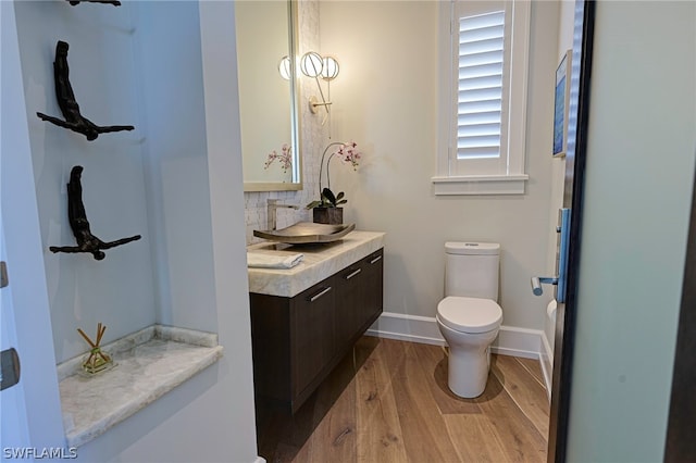 bathroom with wood-type flooring, vanity, toilet, and tasteful backsplash