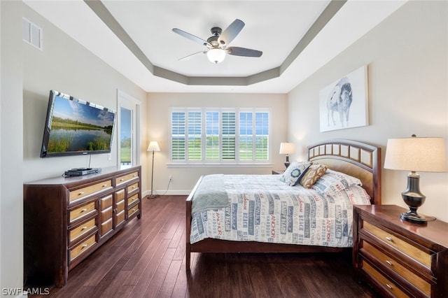 bedroom with ceiling fan, dark hardwood / wood-style floors, and a tray ceiling