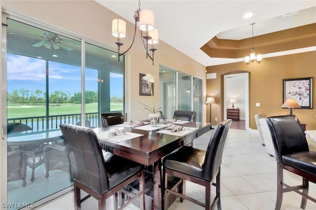 dining room featuring light tile patterned floors, ceiling fan with notable chandelier, and a tray ceiling