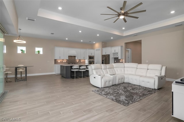 living room with a tray ceiling, ceiling fan, and crown molding