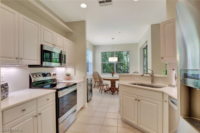 kitchen featuring sink, stainless steel appliances, light tile patterned floors, pendant lighting, and white cabinets