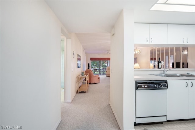 kitchen featuring an inviting chandelier, white dishwasher, sink, light colored carpet, and white cabinetry