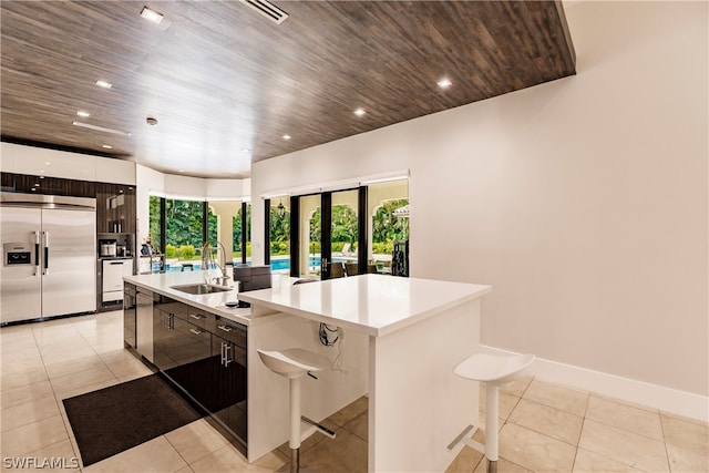 kitchen featuring an island with sink, stainless steel appliances, wood ceiling, light tile floors, and sink