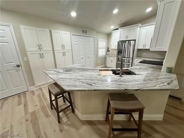 kitchen with a breakfast bar, white cabinets, light hardwood / wood-style floors, stainless steel refrigerator with ice dispenser, and light stone countertops