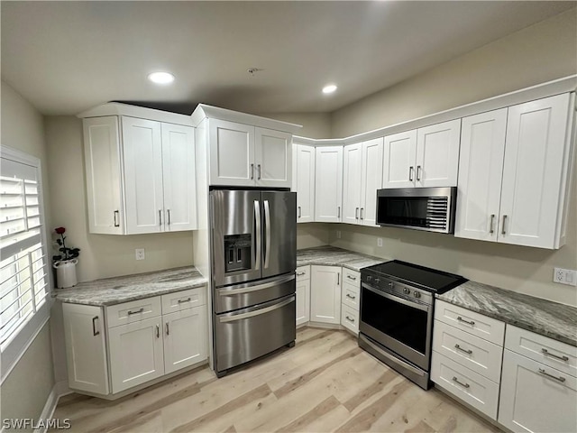 kitchen with light stone countertops, appliances with stainless steel finishes, white cabinets, and light hardwood / wood-style floors