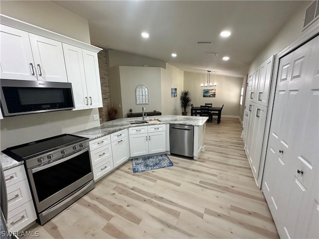 kitchen with light stone counters, stainless steel appliances, kitchen peninsula, and white cabinets