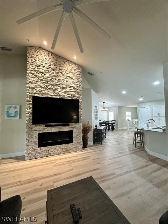 living room with lofted ceiling, a stone fireplace, and light hardwood / wood-style flooring