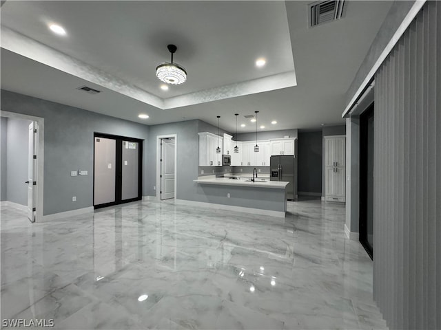 kitchen featuring a tray ceiling, stainless steel appliances, light tile flooring, decorative light fixtures, and white cabinets