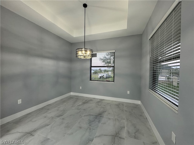 tiled empty room featuring a notable chandelier and a tray ceiling