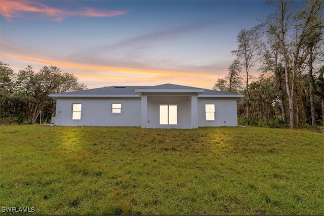 back house at dusk featuring a lawn