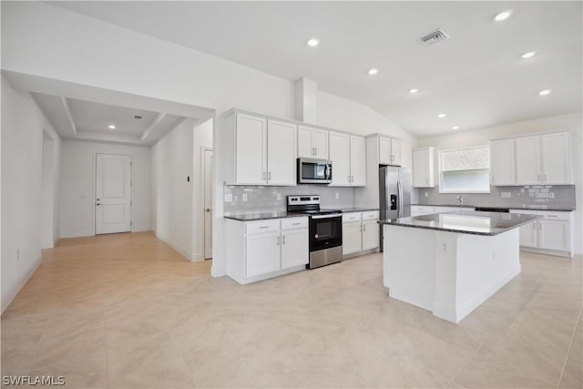 kitchen with appliances with stainless steel finishes, lofted ceiling, white cabinets, and a kitchen island