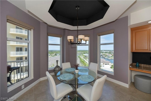 dining room featuring a notable chandelier, a wealth of natural light, a raised ceiling, and light tile patterned flooring