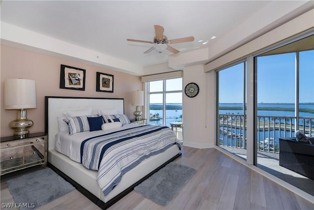 bedroom featuring a water view, access to outside, wood finished floors, baseboards, and ceiling fan