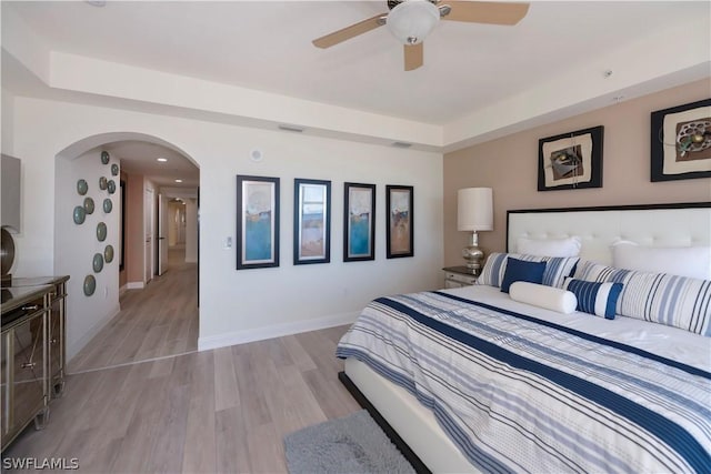 bedroom with a tray ceiling, light hardwood / wood-style floors, and ceiling fan