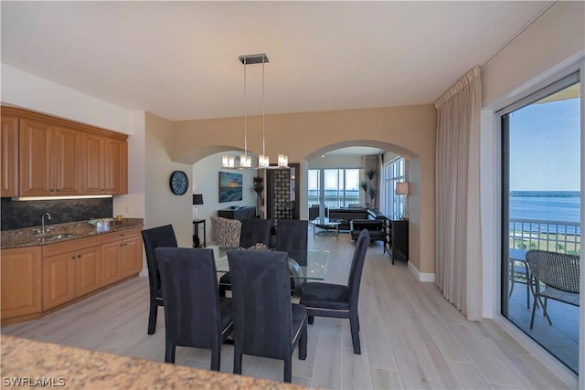 dining area featuring a water view, sink, a chandelier, and light wood-type flooring