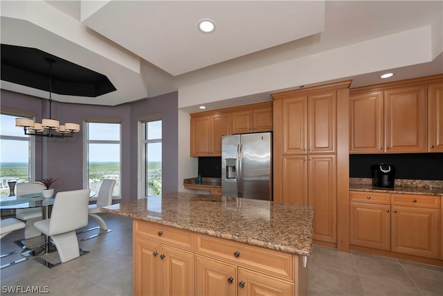 kitchen featuring a kitchen island, decorative light fixtures, stainless steel fridge, light stone counters, and an inviting chandelier