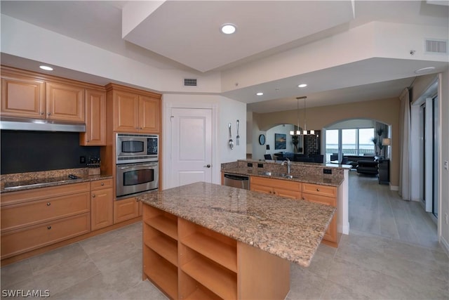 kitchen with sink, light stone counters, decorative light fixtures, a center island, and appliances with stainless steel finishes