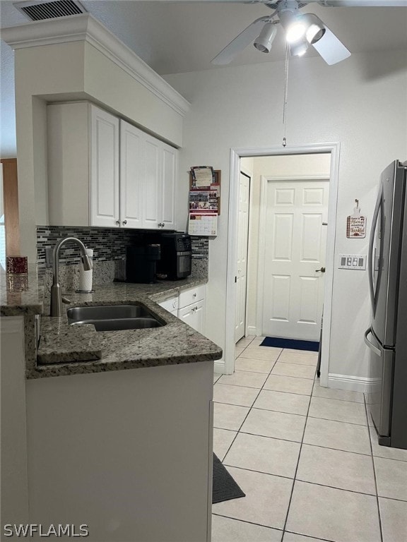 kitchen featuring white cabinetry, stainless steel fridge, dark stone counters, backsplash, and ceiling fan