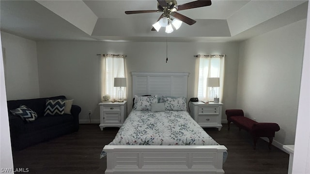 bedroom with ceiling fan, a raised ceiling, and dark wood-type flooring