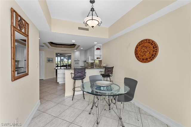 dining area with a raised ceiling and light tile patterned flooring