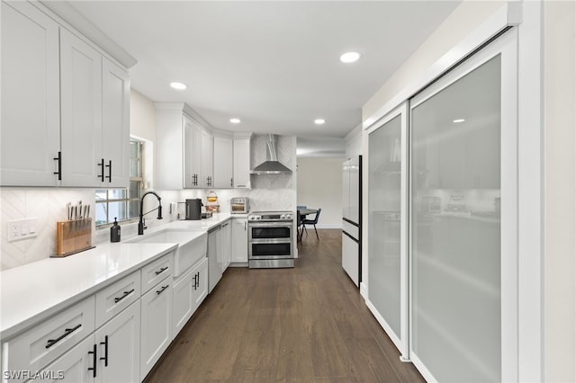 kitchen featuring dishwashing machine, wall chimney exhaust hood, dark wood-style floors, double oven range, and a sink