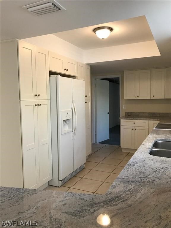 kitchen featuring white cabinets, light tile patterned floors, white fridge with ice dispenser, and sink