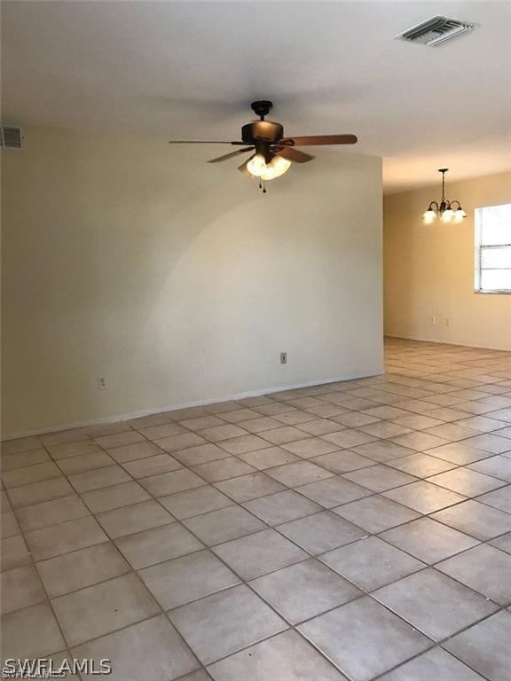 tiled spare room featuring ceiling fan with notable chandelier