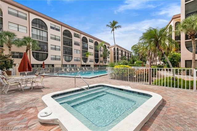 community pool featuring a patio area, fence, and a hot tub