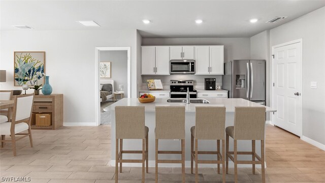 kitchen with stainless steel appliances, a center island with sink, a breakfast bar area, white cabinetry, and light wood-type flooring