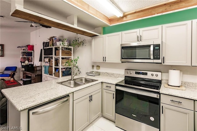 kitchen with stainless steel appliances, light stone counters, a peninsula, and a sink