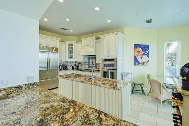 kitchen featuring sink, light tile patterned floors, appliances with stainless steel finishes, light stone counters, and decorative backsplash