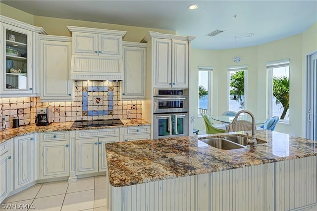 kitchen with double oven, backsplash, light stone countertops, and sink