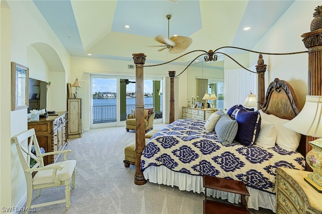 carpeted bedroom with a water view, access to exterior, a tray ceiling, ornate columns, and a high ceiling