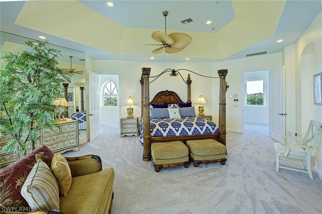 bedroom featuring multiple windows, light colored carpet, and a raised ceiling