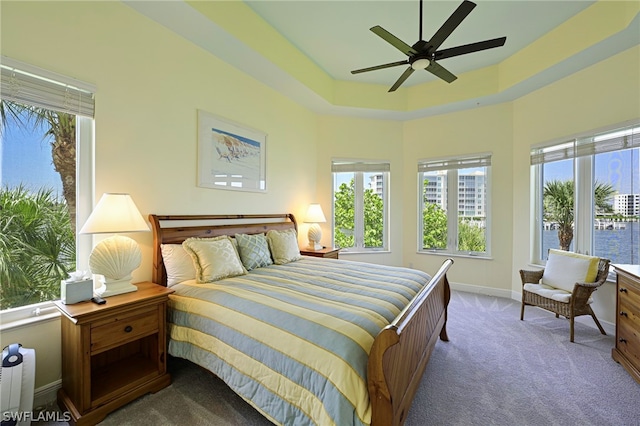 carpeted bedroom with ceiling fan, a raised ceiling, and multiple windows