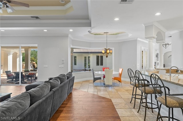 living room with ornamental molding, a tray ceiling, light tile floors, and ceiling fan with notable chandelier