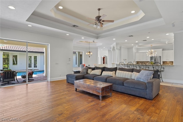 living room featuring a tray ceiling, wood-type flooring, and ceiling fan with notable chandelier