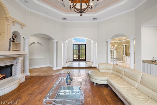 living room featuring a high end fireplace, a raised ceiling, french doors, and an inviting chandelier