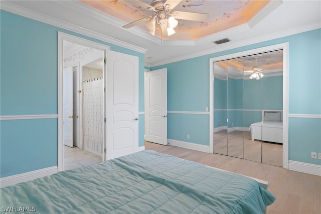 bedroom with a closet, ceiling fan, a raised ceiling, crown molding, and hardwood / wood-style floors