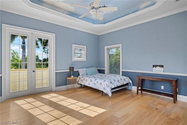 bedroom with light wood-type flooring, a raised ceiling, and multiple windows