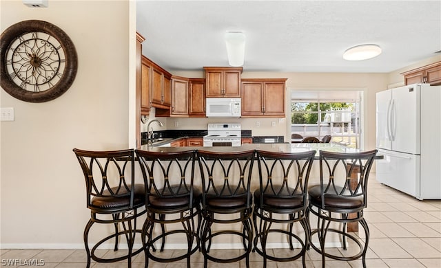 kitchen with a kitchen breakfast bar, sink, light tile flooring, and white appliances