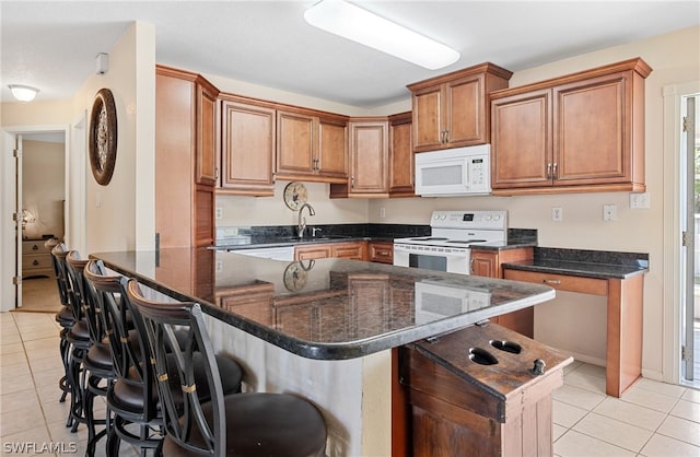 kitchen with dark stone countertops, a breakfast bar area, white appliances, and light tile floors