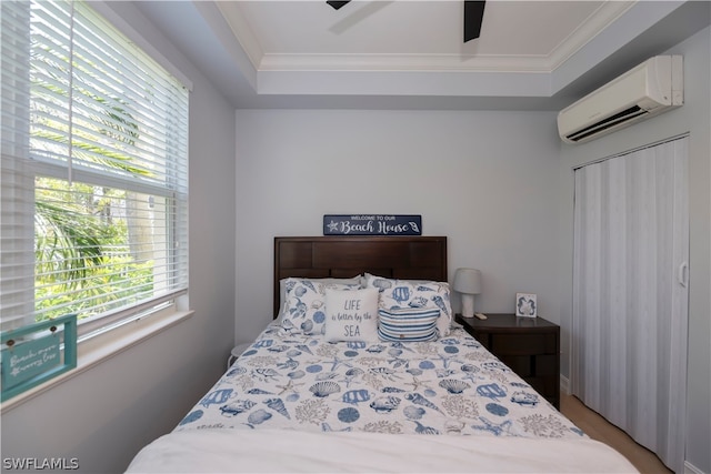 bedroom with a wall unit AC, ceiling fan, and a tray ceiling