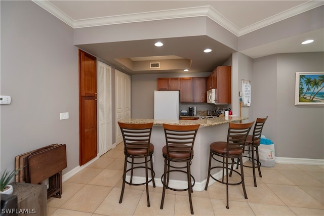 kitchen with light stone countertops, a tray ceiling, kitchen peninsula, white appliances, and light tile flooring