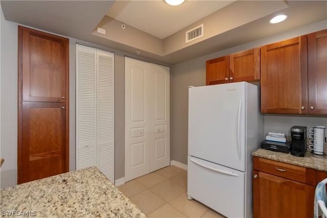 kitchen with light stone countertops, a tray ceiling, white fridge, and light tile floors