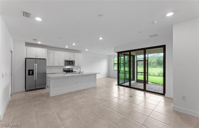 kitchen featuring decorative backsplash, stainless steel appliances, white cabinets, an island with sink, and light tile patterned flooring