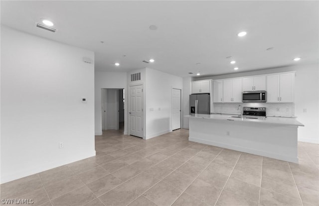 kitchen with decorative backsplash, stainless steel appliances, light tile patterned floors, a center island with sink, and white cabinetry