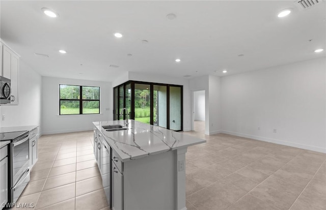 kitchen featuring appliances with stainless steel finishes, light stone counters, sink, a center island with sink, and white cabinetry