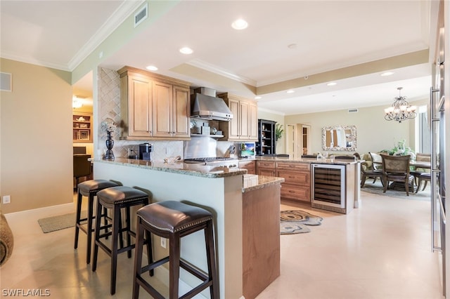 kitchen featuring kitchen peninsula, beverage cooler, wall chimney exhaust hood, and decorative backsplash